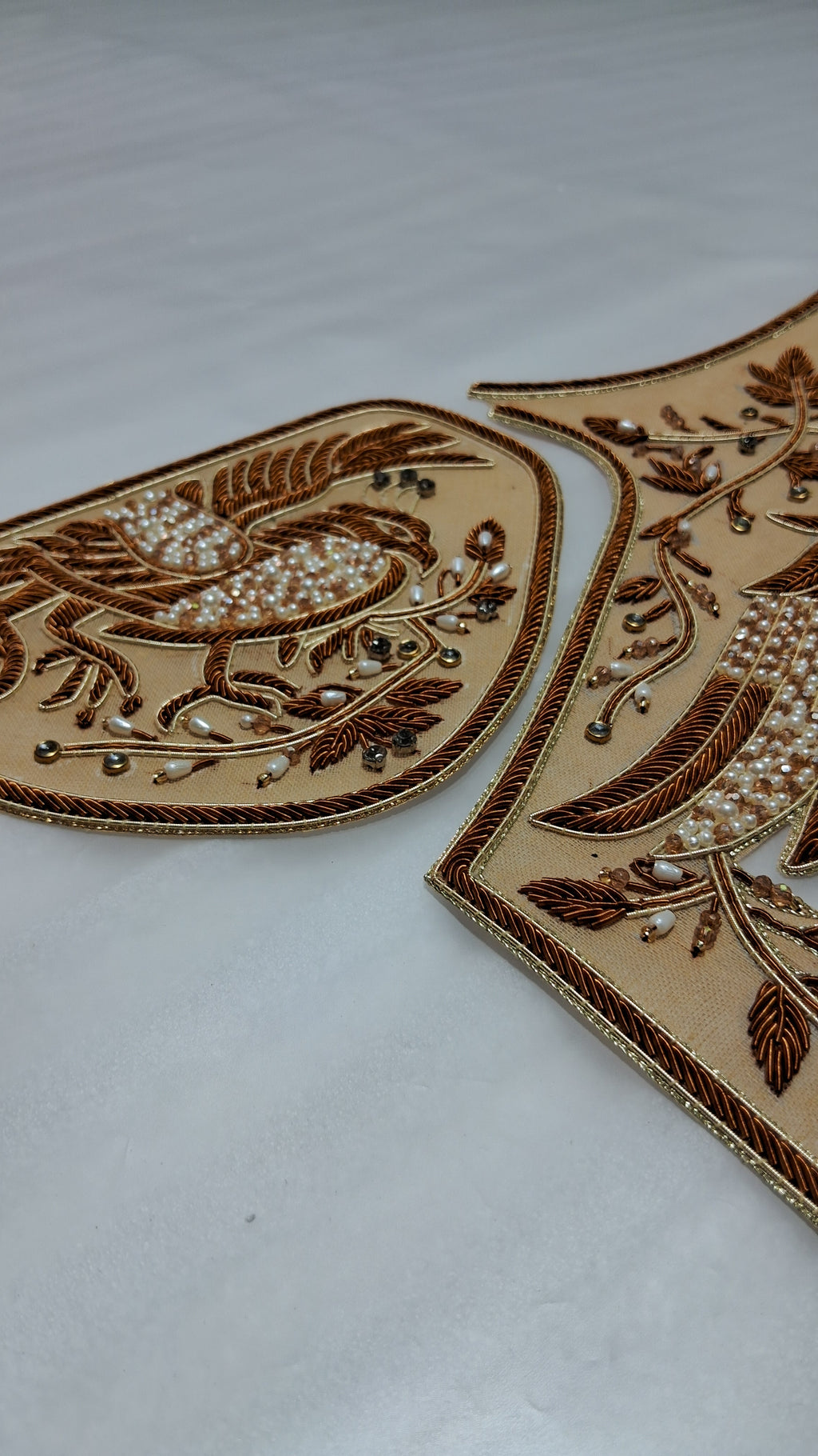 Two embroidered patches with a bird and floral design, featuring brown embroidery, gold metallic thread, and white pearl-like beads on a beige fabric background.