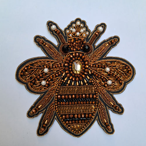 An ornate embroidered bee applique patch featuring intricate metallic gold and bronze beadwork, black outlines, and small white pearl accents on a light gray background.