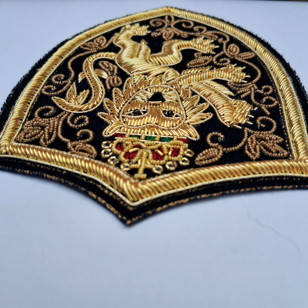 An embroidered patch featuring a golden dragon and crest design on a black background, with red and green jewel accents, photographed on a light gray surface.