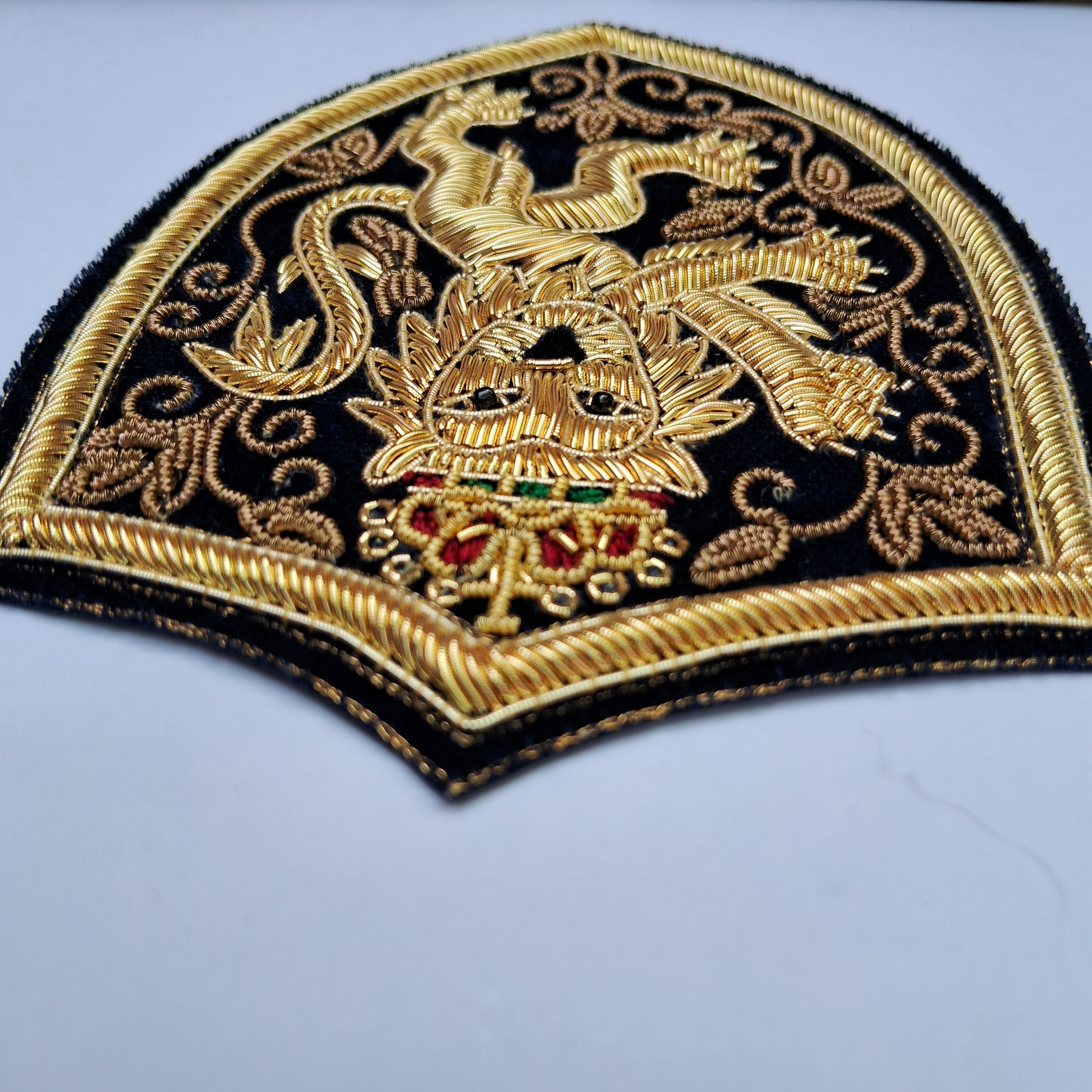 An embroidered patch featuring a golden dragon and crest design on a black background, with red and green jewel accents, photographed on a light gray surface.