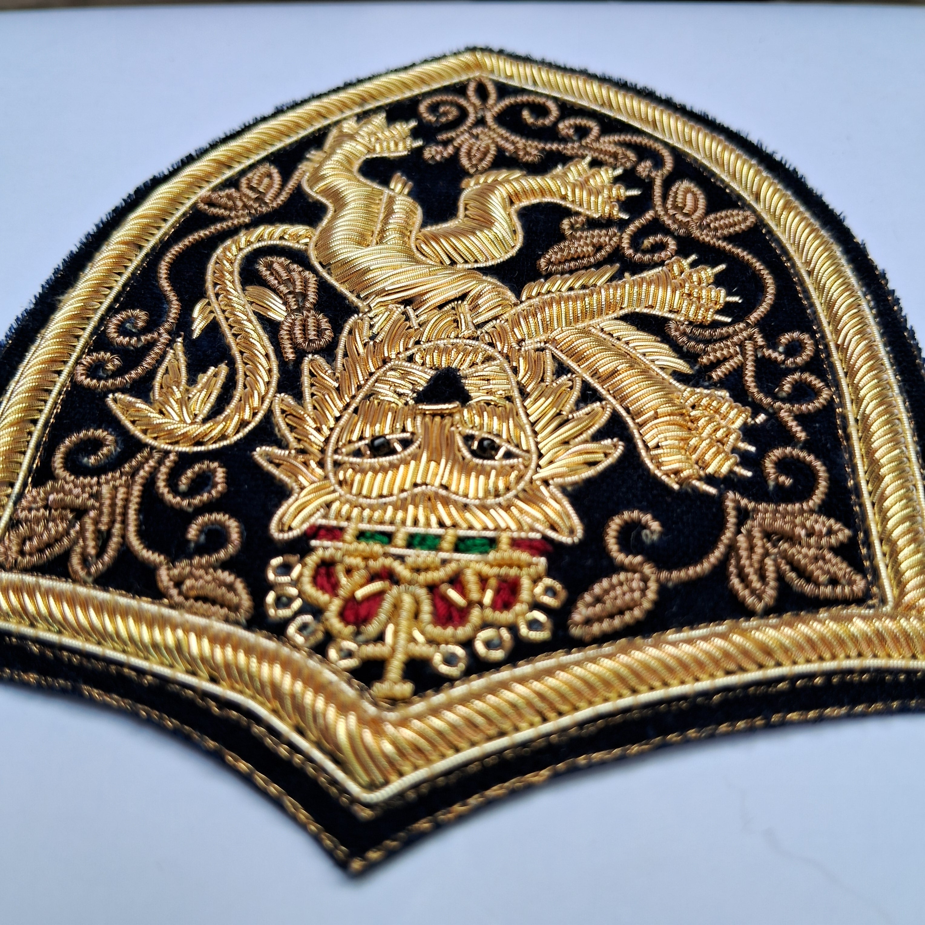 Close-up of an embroidered decorative patch featuring a gold phoenix and crown motif on a black background with red and green accents.