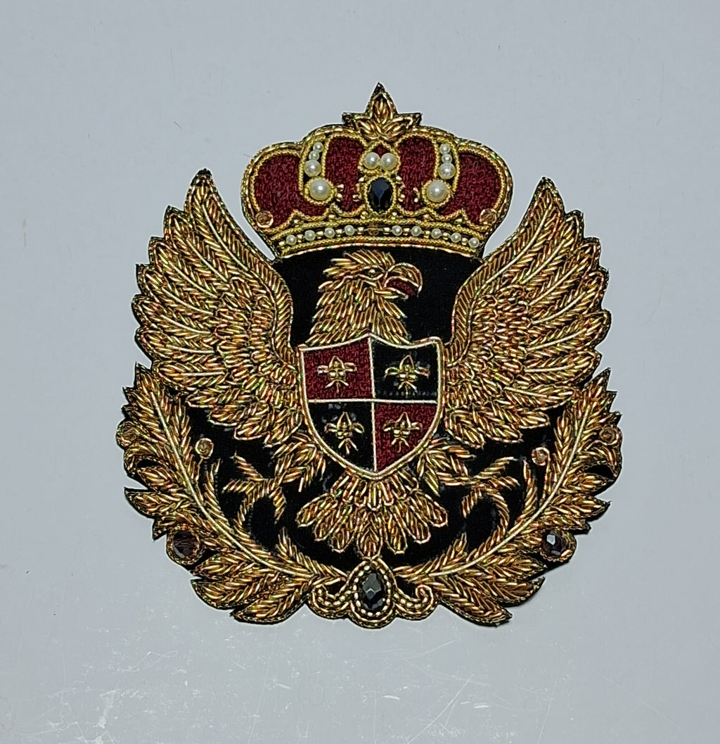 An ornate embroidered crest patch featuring a double-headed eagle under a crown, with gold threadwork, black enamel, and red details on a light gray background.